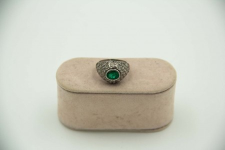 Anel de platina com lascas de diamante e aplicação de esmeralda no centro.