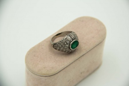 Anel de platina com lascas de diamante e aplicação de esmeralda no centro.