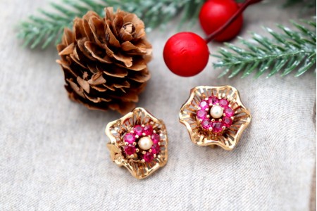 Brincos em ouro em forma de flor com pedras sintéticas vermelhas e pérolas no centro.