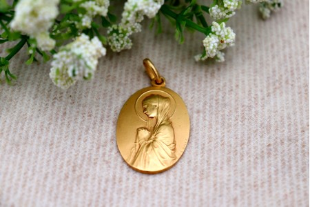 Medalha em ouro com Nossa Senhora orando em vulto perfeito relevado e argola de suspensão.