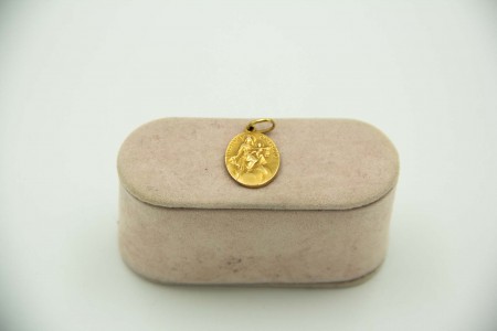 Medalha ilíptica em ouro amarelo com Nossa Senhora e menino em relevo.