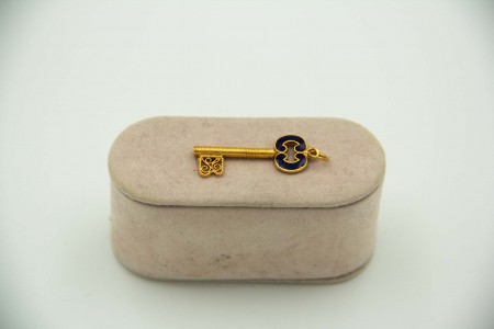 Medalha de ouro amarelo em forma de chave com esmaltes policromados aplicados.