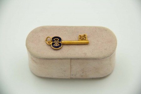 Medalha de ouro amarelo em forma de chave com esmaltes policromados aplicados.