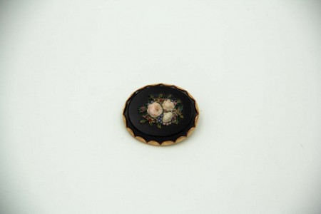 Pregadeira oval com aro em ouro recortado envolvendo onix com rosas relevadas