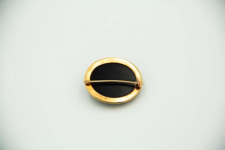 Pregadeira oval com aro em ouro recortado envolvendo onix com rosas relevadas