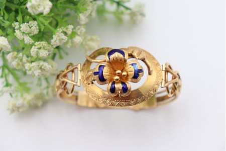 Pulseira em ouro com relevos e aplicações com flor no centro esmaltada