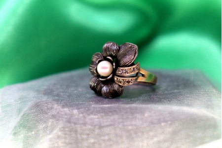 Anel em ouro e prata em forma de flor com pedras incolores e pérola no centro.