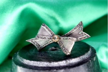 Pregadeira em ouro e prata em forma de laço com lascas de diamantes.