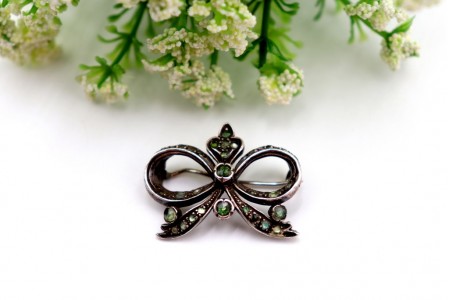 Pregadeira em ouro e prata em forma de laço com lascas de diamantes e esmeraldas