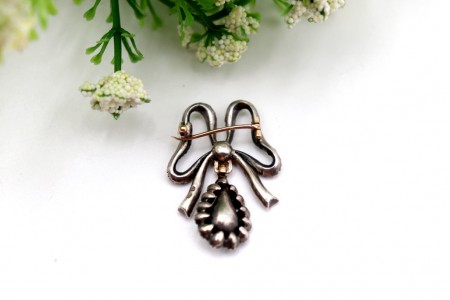 Pregadeira em ouro e prata em forma de laço com pingente articulado.