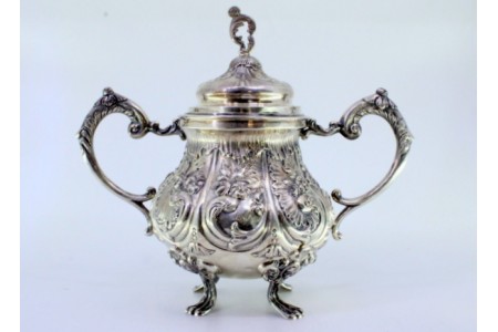 Açucareiro em prata relevada com motivos florais, folhas de acanto e assente sobre quatro pés em forma de garras.