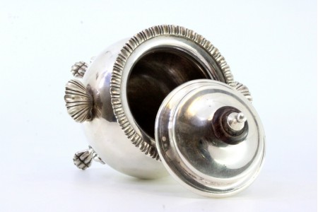 Açucareiro em prata com duas pegas em forma de concha, corpo liso,  pomo de madeira,na tampa, friso no bordo e assente em quatro pés em forma de garras.