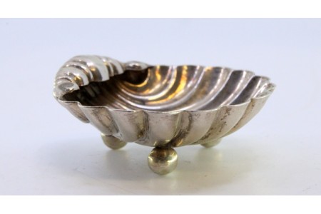 Aneleira em prata em forma de concha canelada com três pés em forma de bola.