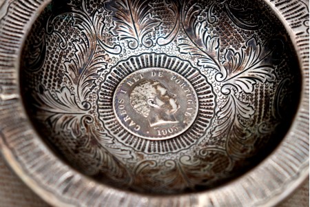 Aneleira em prata com relevos em formato circular com moeda do Rei D. Carlos I e assente em três pés alteados.