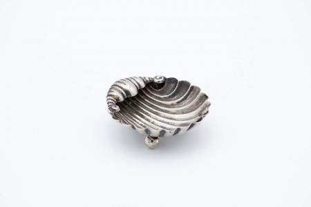 Aneleira em forma de concha em prata canelada e assente em três pés esféricos.  Aneleira em forma de concha em prata canelada e assente em três pés esféricos.