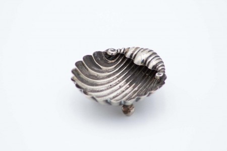 Aneleira em forma de concha em prata canelada e assente em três pés esféricos.  Aneleira em forma de concha em prata canelada e assente em três pés esféricos.