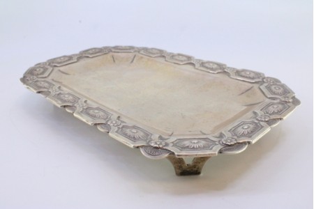 Bandeja em prata em forma retangular de cantos cortados e relevos florais na envolvência, assente sobre quatro pés vazados.