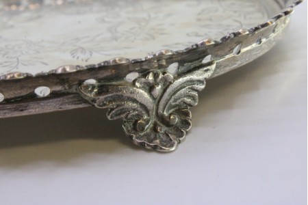 Bandeja em prata com gradinha e motivos florais gravados no fundo com três pés relevados.