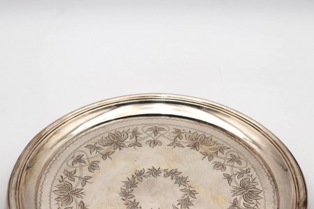 Bandeja/bilheteira de prata em forma circular com motivos florais gravados.