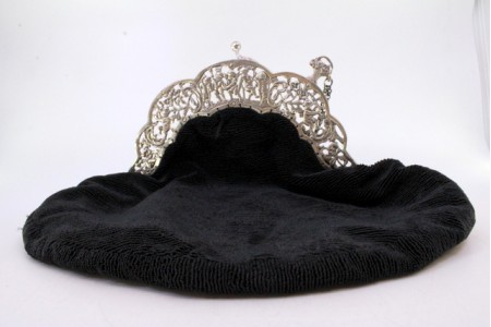 Bolsa de mão em prata no arco recortado com figuras angélicas e motivos florais suportando a bolsa de tecido que forra o interior.