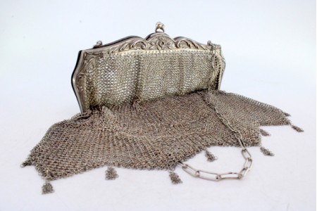 Bolsa de mão em malha de prata com franjas suspensas, arco relevado com motivos florais e corrente em malha cadeado.