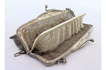   Bolsa em malha dupla de prata com duas divisórias no interior, franjas suspensas, arco com motivos florais recortados e corrente em malha cadeado.