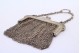 Bolsa de mão em malha de prata com arco relevado e corrente em malha cadeado.