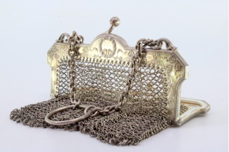 Bolsa de mão em malha de prata com arco relevado e corrente em malha cadeado.