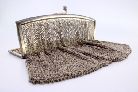 Bolsa de mão em malha de prata com arco liso  e fecho em forma de bolas.