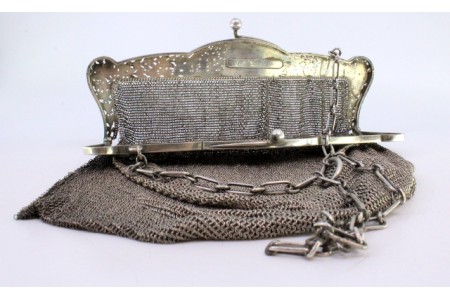 Bolsa de mão em prata com relevos no arco com cartela para monograma e corrente de transporte.