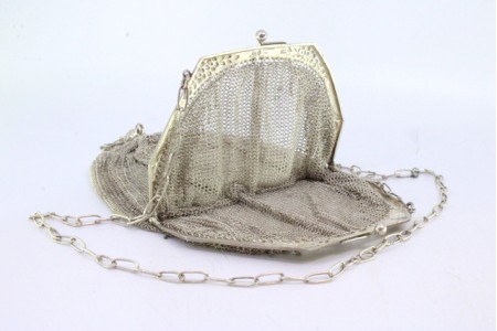 Bolsa de mão em malha de prata com franjas suspensas, relevos e aplicações no arco, corrente em malha cadeado.