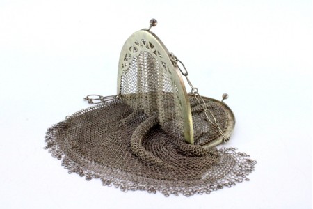 Bolsa de mão em malha de prata com arco recortado, franjas pendentes e corrente em malha cadeado.