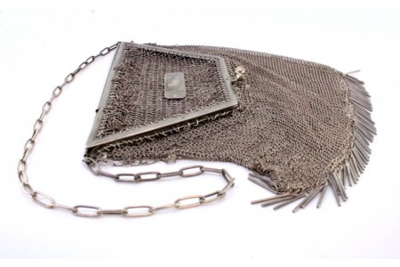 Bolsa de mão em malha de prata com arco em forma de trapésio, franjas pendentes e corrente em malha cadeado.