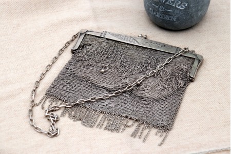 Bolsa em malha de prata com dois pingentes em forma de bola e cadilhes articulados, interior forrado a tecido,  arco com relevos e corrente em malha cadeado.