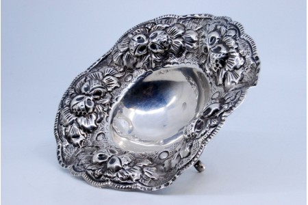 Bomboneira em prata com relevos e aplicações com motivos florais e três pés de apoio.