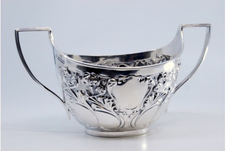 Bomboneira em prata relevada com motivos florais, volutas envolvendo cartelas para monogramas.