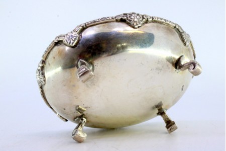 Bomboneira em prata com frisos relevados e pomo de três flores na tampa, assente em três pés decorados com palmas.