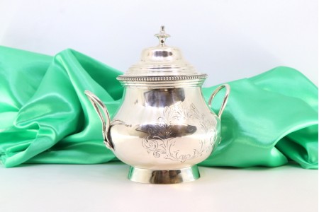 Açucareiro em prata com rebordo perlado, tampa amovível com pomo, asas vazadas e base circular.