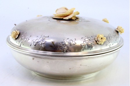 Bomboneira em prata de forma circular com relevos florais na tampa e pomo em forma de flor.