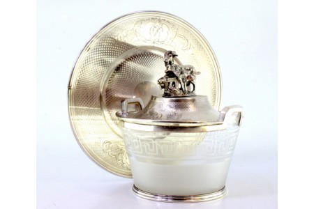 Bomboneira em prata com prato e tampa guilhochados, pomo com cabra pastando, cartelas para monogramas e alma em vidro fosco com friso grego na envolvência.