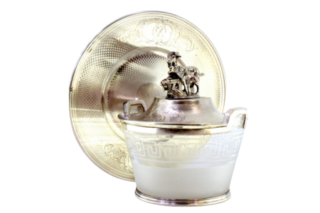 Bomboneira em prata com prato e tampa guilhochados, pomo com cabra pastando, cartelas para monogramas e alma em vidro fosco com friso grego na envolvência.