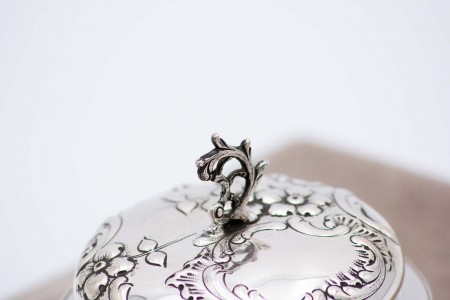 Bomboneira em vidro facetado com tampa em prata relevada com motivos florais e pomo recortado.