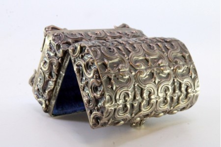 Caixa de prata relevada em forma de báu e interior forrado a veludo azul.