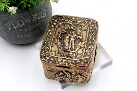 Caixa em prata dourada com relevos idilicos com casal no centro e tampa basculante.