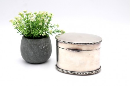 Caixa para chá em prata lisa de formato iliptíco com friso perlado na tampa e base com quatro pés circulares.