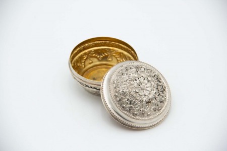 Caixa de forma circular em prata com relevos de flores na tampa dourada