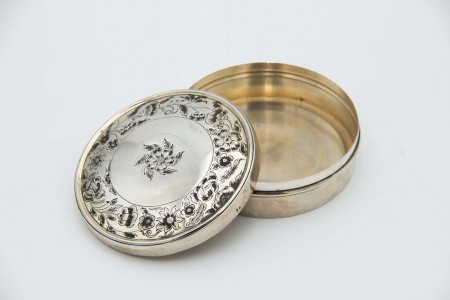 Caixa de prata em formato cilíndrico com motivos floraais relevados na tampa amovível.