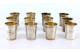 Conjunto de doze copos pra vodka em prata com relevos florais envolvendo cartelas para monogramas e interior em dourado.