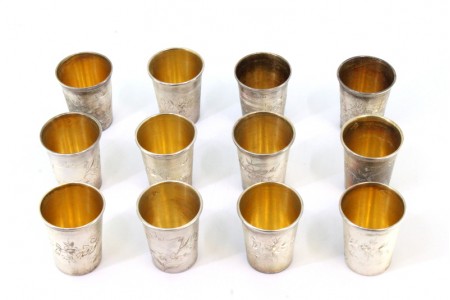 Conjunto de doze copos pra vodka em prata com relevos florais envolvendo cartelas para monogramas e interior em dourado.