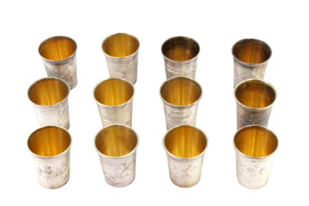 Conjunto de doze copos pra vodka em prata com relevos florais envolvendo cartelas para monogramas e interior em dourado.